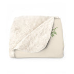 A folded Cream sherpa fleece blanket for Mom shows the fluffy cream back beside a green leafy sprig on the printed front.