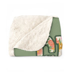 A folded Sage sherpa fleece blanket has a corner turned back, showing its fluffy cream sherpa back beside the floral front.