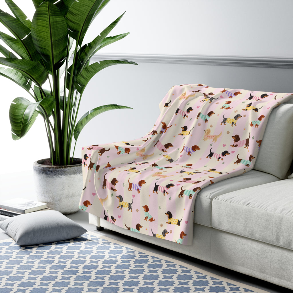 Pink stripes sherpa fleece blanket on a sofa arm beside a plant, showing sweater dogs on soft cream and blush bands.