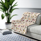 Sofa arm draped with a Cream sherpa fleece blanket beside a potted plant, showing dachshunds in knit sweaters.