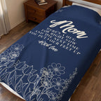 A Navy Mother's Day blanket in velveteen plush covers a single dark wooden bed, showing "Mom", the message and a cream wildflower meadow.