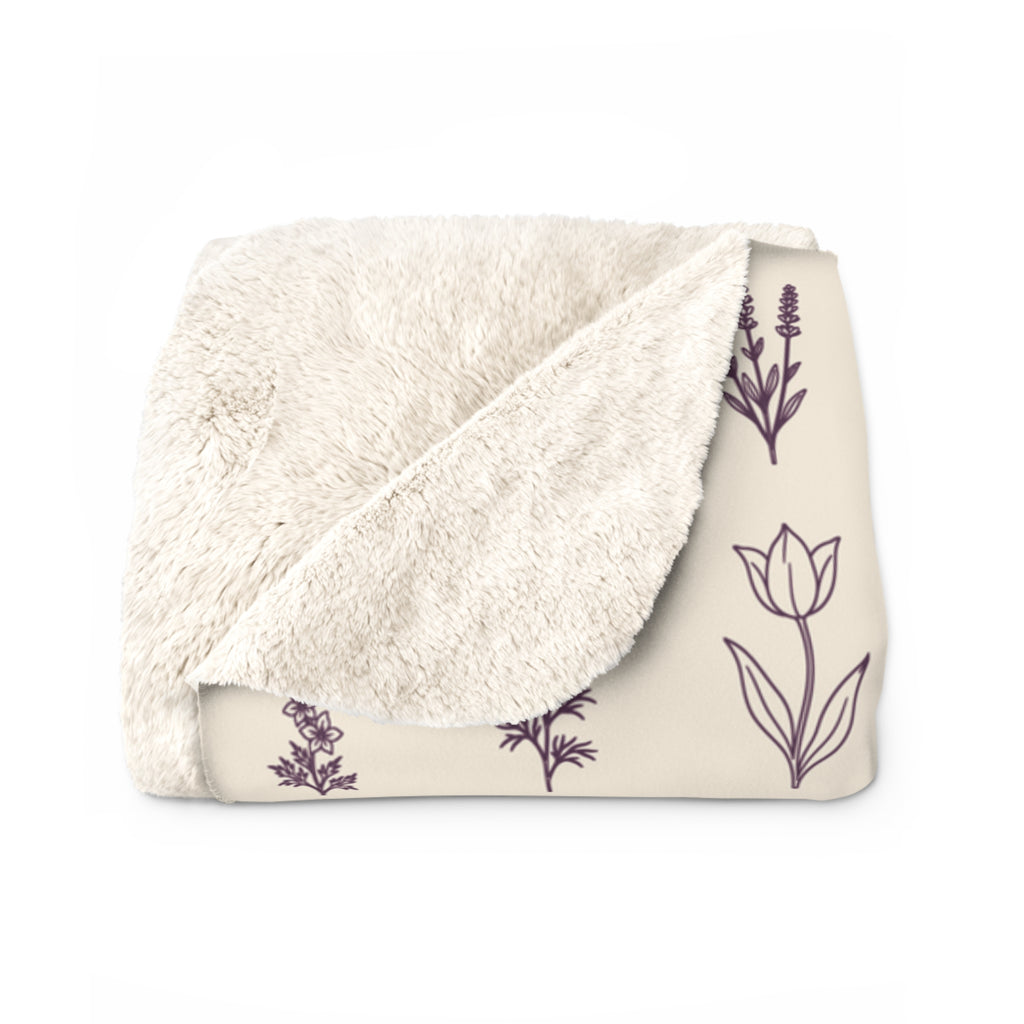 Folded corner of a Cream wildflower blanket in sherpa fleece reveals its fluffy cream back beside a deep plum tulip and lavender stem.