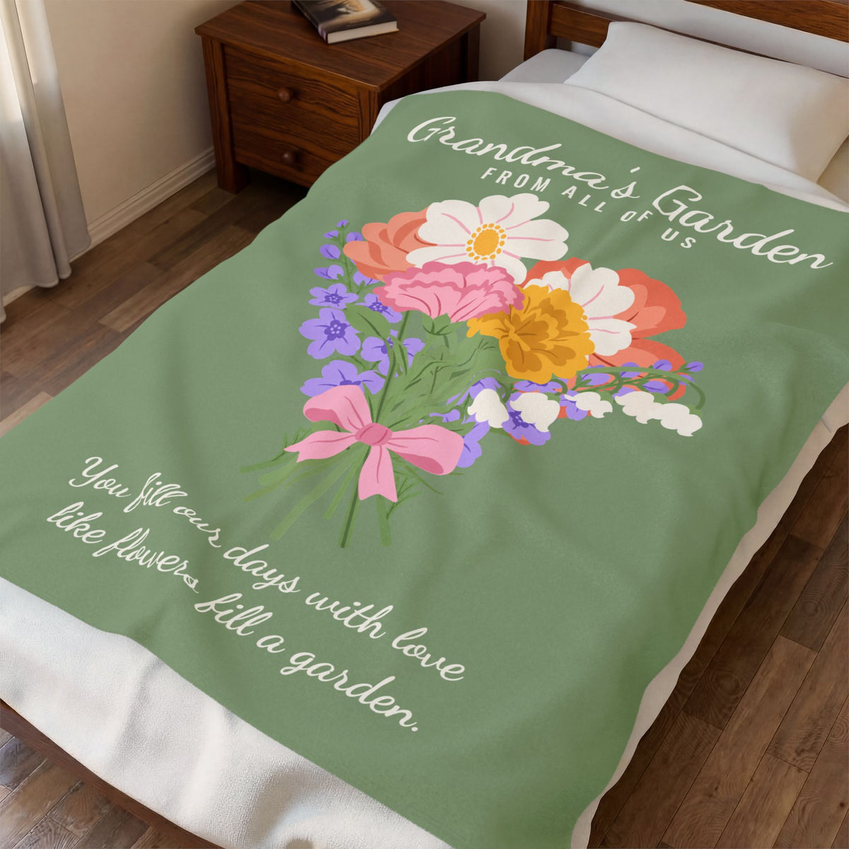 Seen from the foot of a made bed, a Sage velveteen plush blanket shows "Grandma's Garden" and a bouquet beside a wooden nightstand.