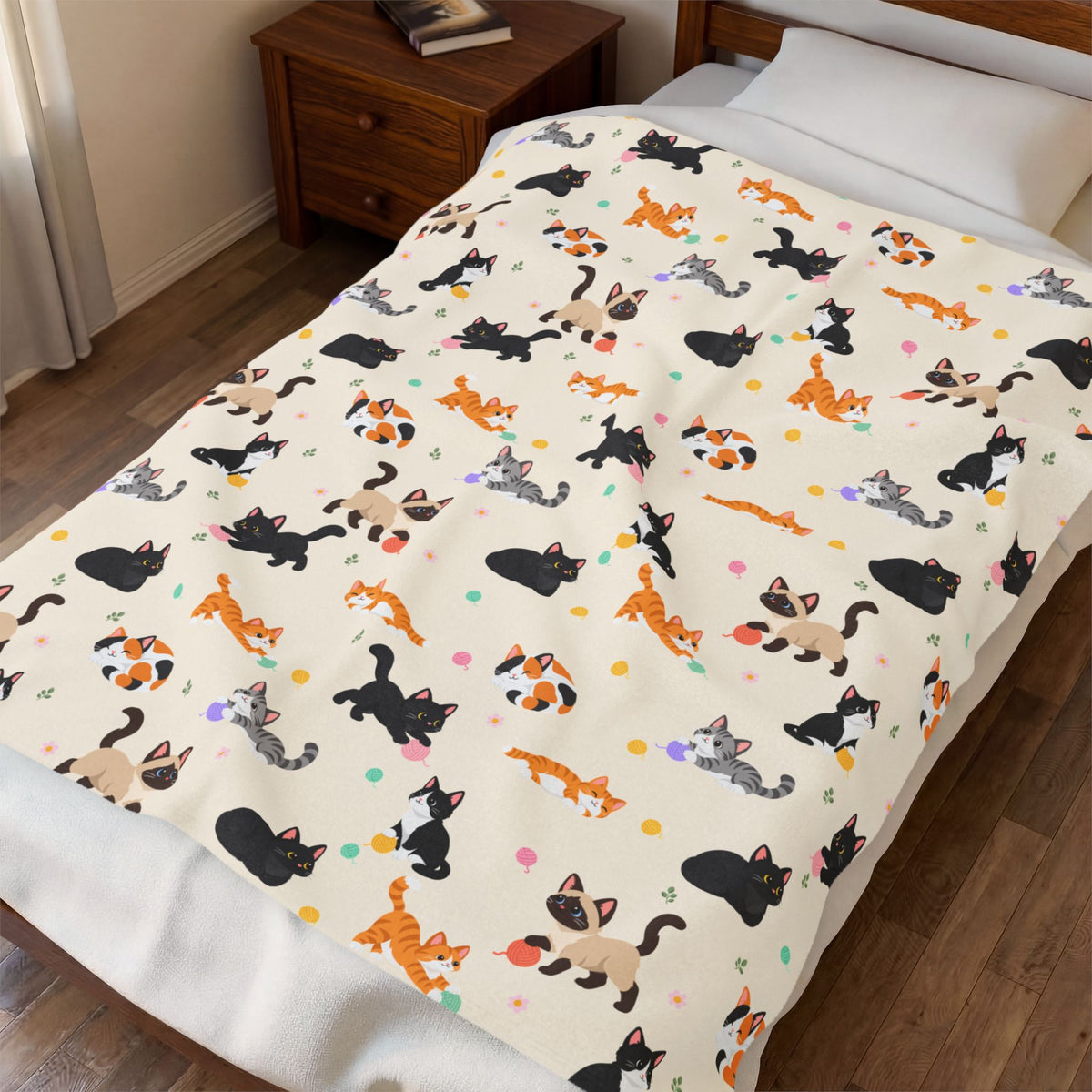 Viewed from above at an angle, a Cream velveteen plush blanket with cartoon cats covers a made bed beside a wooden nightstand.