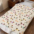 Made bed with a Cream velveteen plush blanket draped across it, showing the repeated dachshunds in knit sweaters.