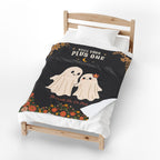 A turned corner reveals the plain white back of a Black velveteen plush blanket beside its two cream ghosts on a light wooden bed.