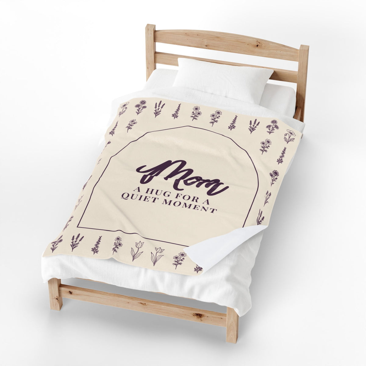 On a single wooden bed, a Cream mom hug blanket in velveteen plush has one corner folded back to show the plain white back.