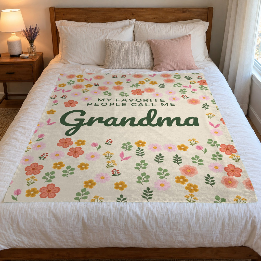 On a wooden queen bed, a 50 x 60 inch Cream velveteen plush blanket shows little flowers and "Grandma" script against white bedding.