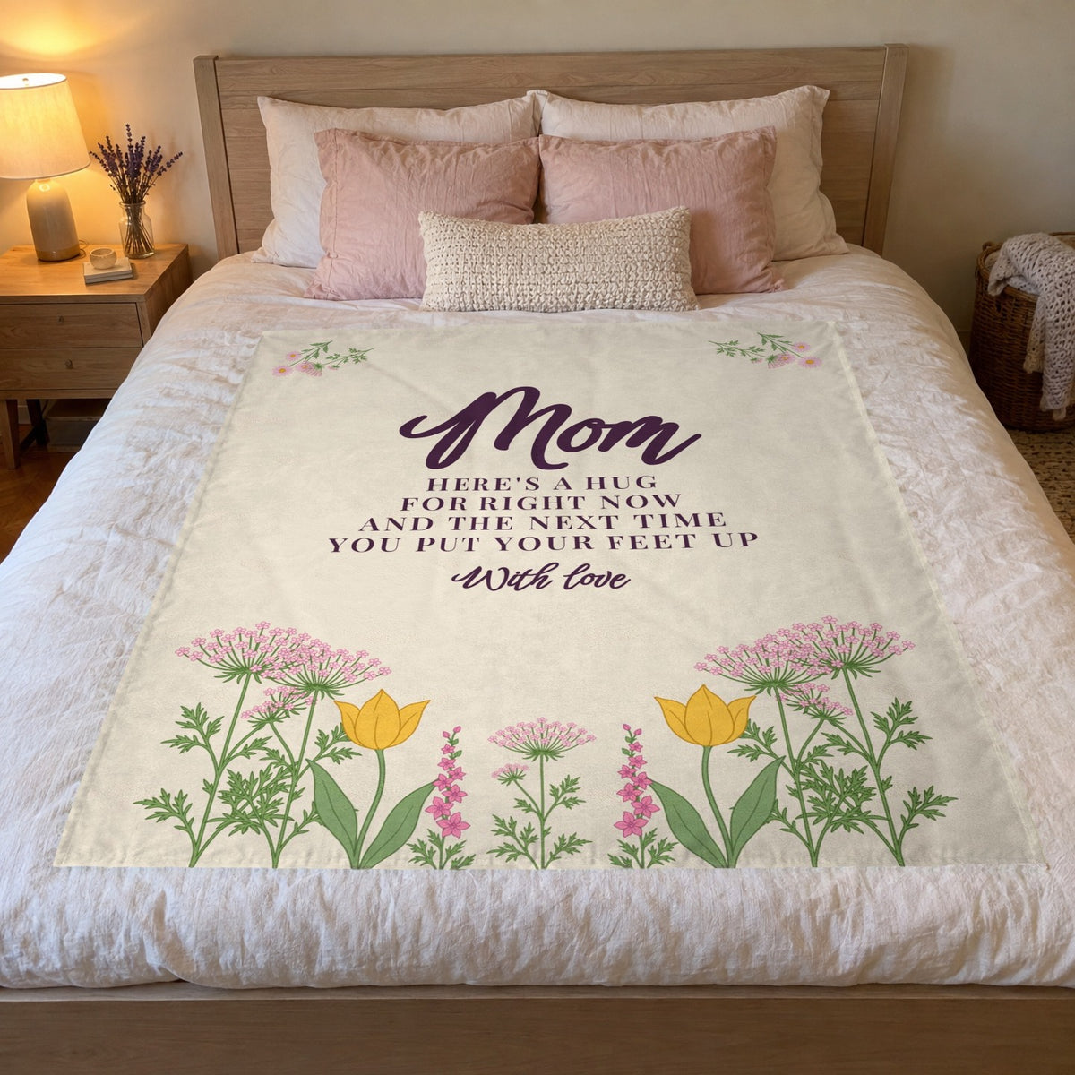 On a queen bed, a 50 x 60 inch Cream Mother's Day gift blanket in velveteen plush lies beside blush pillows and a glowing bedside lamp.