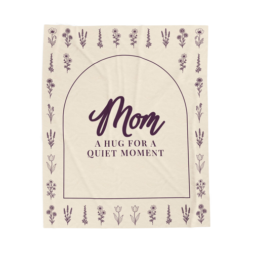 A Cream hug blanket in velveteen plush lies flat on white, showing "Mom" and "A hug for a quiet moment" inside a deep plum arch with flower rows.