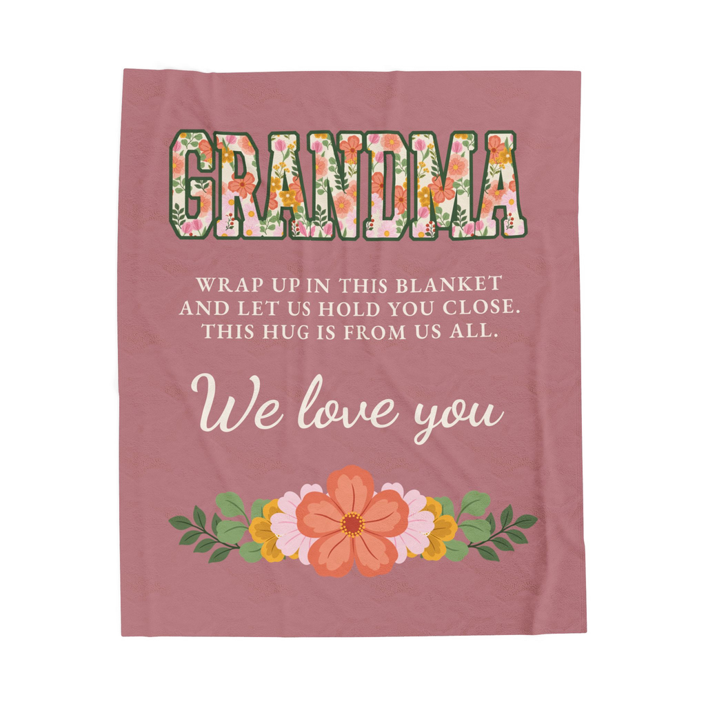 Laid flat on white, a Dusty rose blanket for grandma in velveteen plush shows floral "GRANDMA" above "THIS HUG IS FROM US ALL."