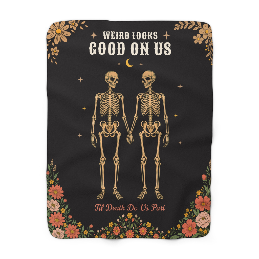 Two tan skeletons hold hands on a Black sherpa fleece blanket laid flat on white, with cream capitals and rounded corners.