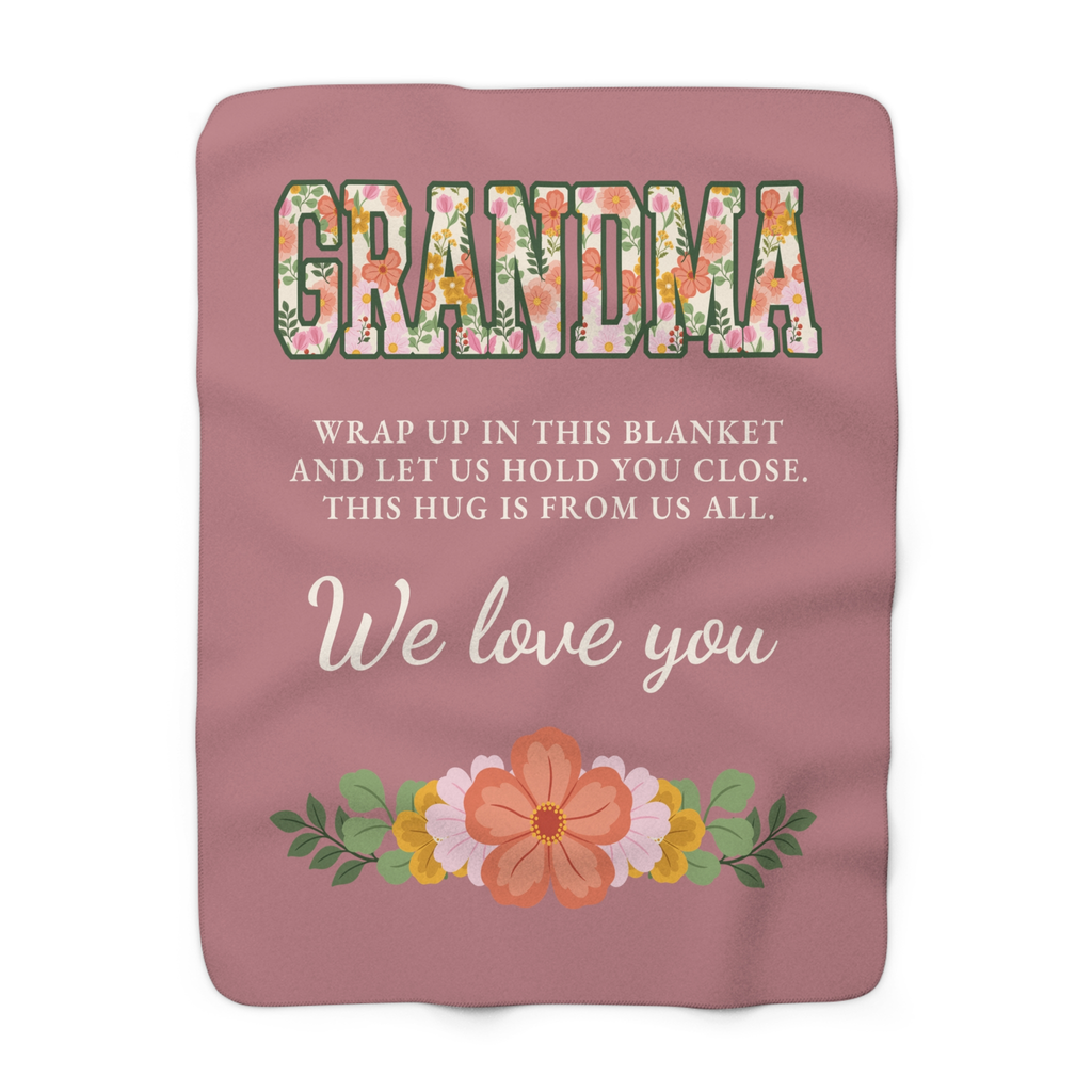Laid flat on white, a Dusty rose grandma hug blanket in sherpa fleece shows floral letters and "THIS HUG IS FROM US ALL."