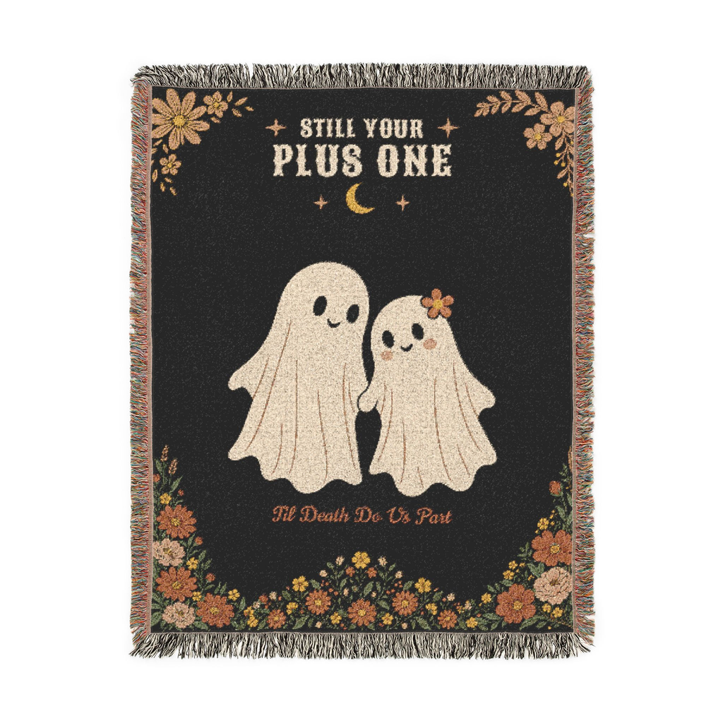Two cream ghosts, one with a flower on her head, appear on a Black woven cotton blanket laid flat on white, with fringe on all four sides.