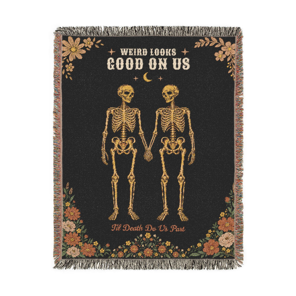 Fringe borders the Black gothic throw blanket in woven cotton, laid flat on white with two skeletons holding hands and wildflowers.