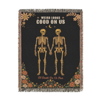Fringe borders the Black gothic throw blanket in woven cotton, laid flat on white with two skeletons holding hands and wildflowers.