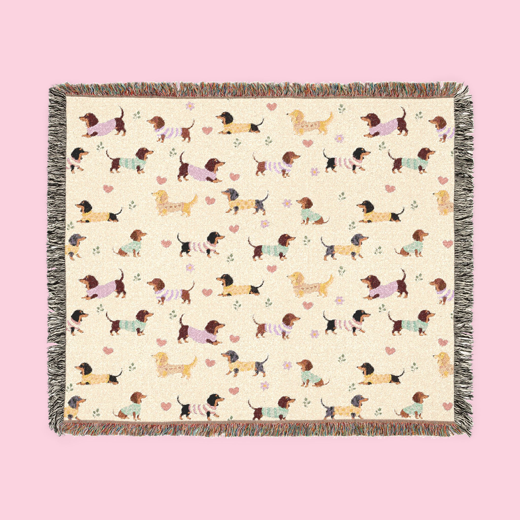 Colorful fringe borders a Cream woven cotton blanket laid flat, showing dachshunds in knit sweaters.