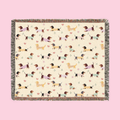 Colorful fringe borders a Cream woven cotton blanket laid flat, showing dachshunds in knit sweaters.