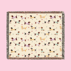 Colorful fringe borders a Cream woven cotton blanket laid flat, showing dachshunds in knit sweaters.