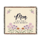 Cream mom throw blanket in woven cotton, 60 x 50 inches, lies flat on white with soft lilac wildflowers, green stems and fringe.