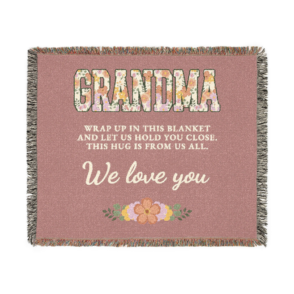 Laid flat on white, a Dusty rose grandma throw blanket in woven cotton shows floral "GRANDMA", cream script and fringe on all four sides.