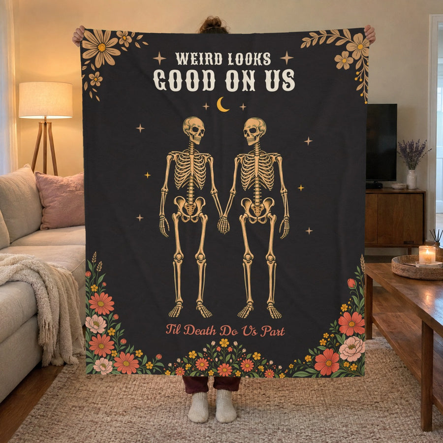 A woman holds up a 50 x 60 inch Black velveteen plush blanket with a skeleton couple in a media room with warm lamp light.
