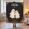 By a family room bay window, a woman holds up a 50 x 60 inch Black velveteen plush ghost blanket showing two smiling cream ghosts.