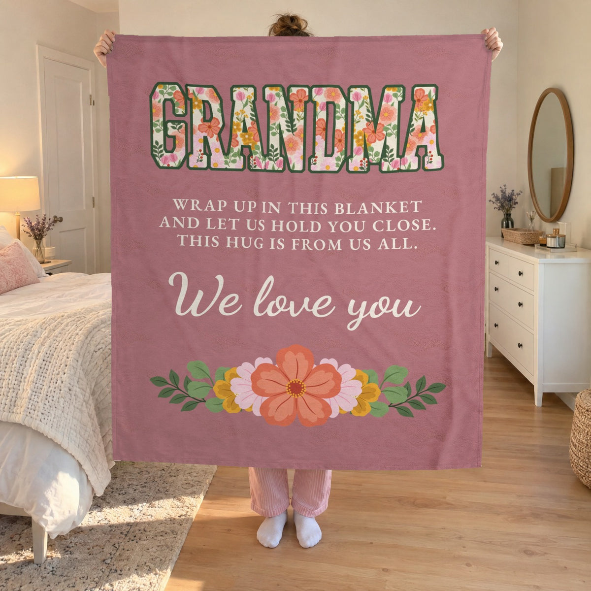 In a bright bedroom, a woman holds up a 50 x 60 inch Dusty rose velveteen plush blanket, with pink pajama pants visible below.
