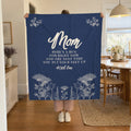 A woman holds up a 50 x 60 inch Navy velveteen plush blanket with cream flowers in a bright dining nook with a round white table.