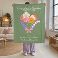 In a bright loft living room, a woman holds up a 50 x 60 inch Sage Grandma's Garden blanket in velveteen plush against white brick walls.