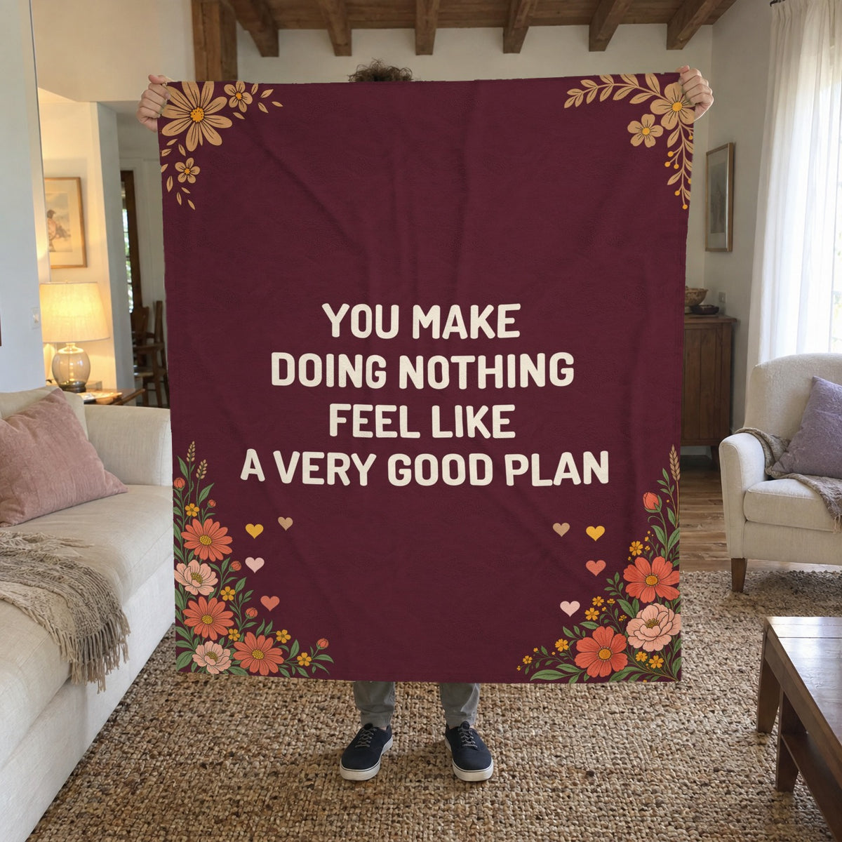 A man holds up a 50 x 60 inch Wine velveteen plush love letter blanket with cream words in a living room with a wooden beam ceiling.