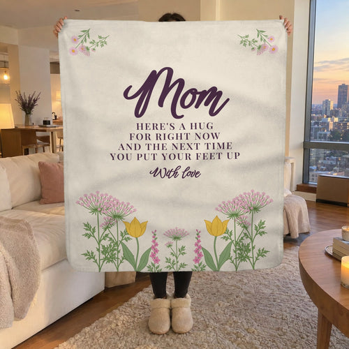 In a living room overlooking the city at dusk, a woman holds up a 50 x 60 inch Cream sherpa fleece blanket with a wildflower meadow.