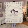 A woman holds up a 50 x 60 inch Cream sherpa fleece blanket with an arch and flower rows in a living room with soft lilac walls.