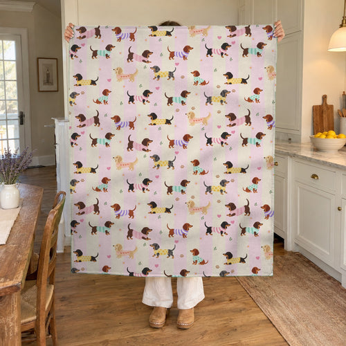 In a sunny kitchen, a woman holds up a 50 x 60 inch Pink stripes sherpa fleece dachshund blanket near a bowl of lemons.