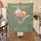 A woman holds up a 50 x 60 inch Sage sherpa fleece blanket in a sunny kitchen beside a wooden table, white cabinets and a bowl of lemons.
