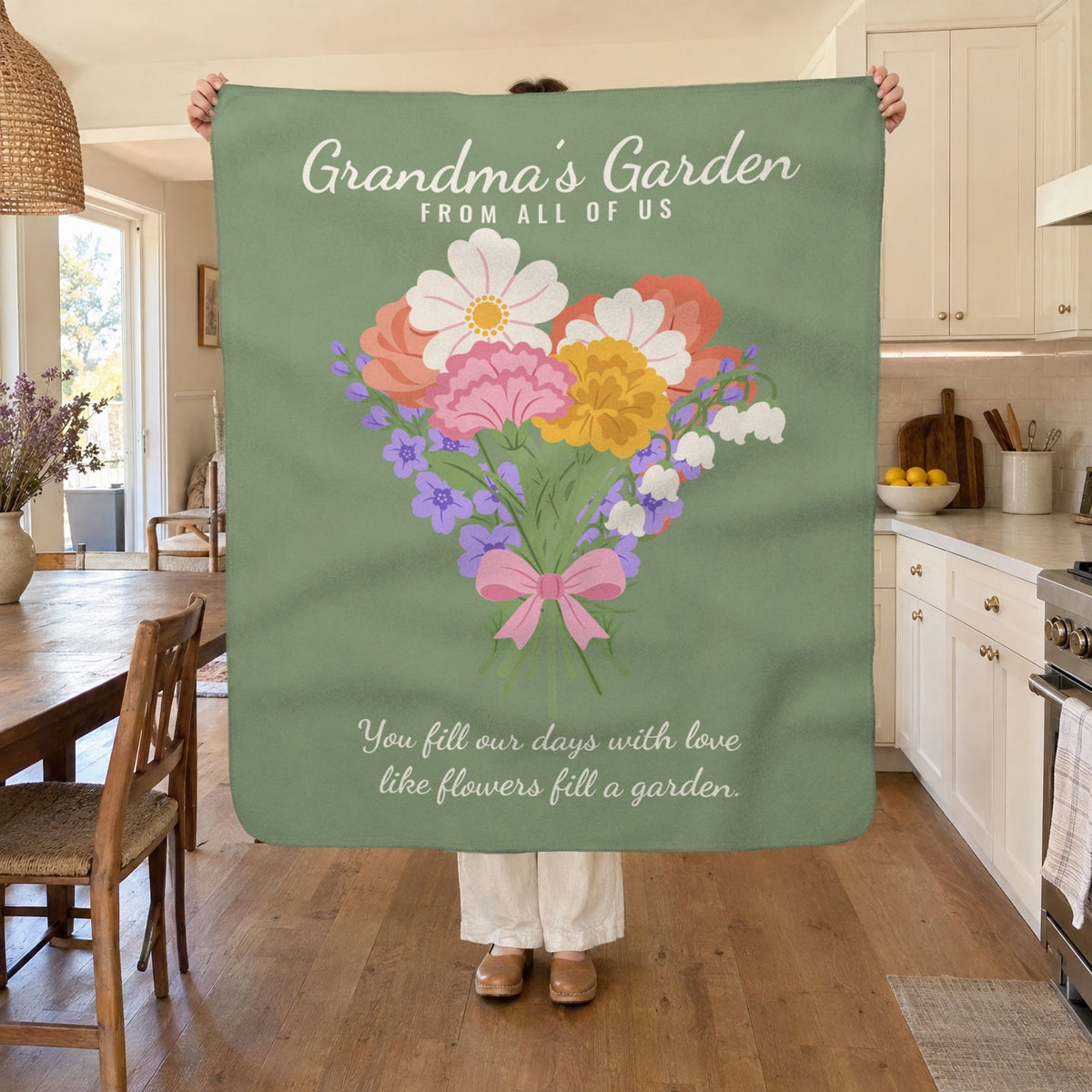 A woman holds up a 50 x 60 inch Sage sherpa fleece blanket in a sunny kitchen beside a wooden table, white cabinets and a bowl of lemons.
