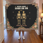 A man holds up a fringed 60 x 50 inch Black woven cotton blanket with two skeletons in a hallway with soft painted walls.