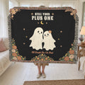 In a sunroom, a woman holds up a fringed 60 x 50 inch Black woven cotton ghost throw blanket beside a cream daybed and sheer curtains.