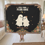 In a sunroom, a woman holds up a fringed 60 x 50 inch Black woven cotton ghost throw blanket beside a cream daybed and sheer curtains.