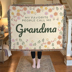 A woman holds up a fringed 60 x 50 inch Cream woven cotton blanket in an entryway beside a wooden staircase with a white banister.