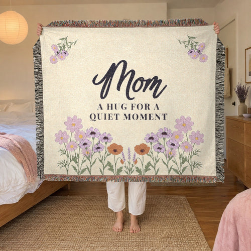 In a bedroom with a low oak bed and paper lantern lamp, a woman holds up a fringed 60 x 50 inch Cream woven cotton blanket.