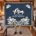 A man holds up a fringed 60 x 50 inch Navy woven cotton blanket with cream flowers in a living room with wood walls and a stone fireplace.