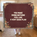 A woman holds up a fringed 60 x 50 inch Wine woven cotton anniversary blanket with cream words in a bedroom with cream bedding.
