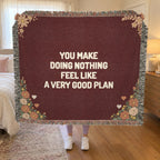 A woman holds up a fringed 60 x 50 inch Wine woven cotton anniversary blanket with cream words in a bedroom with cream bedding.