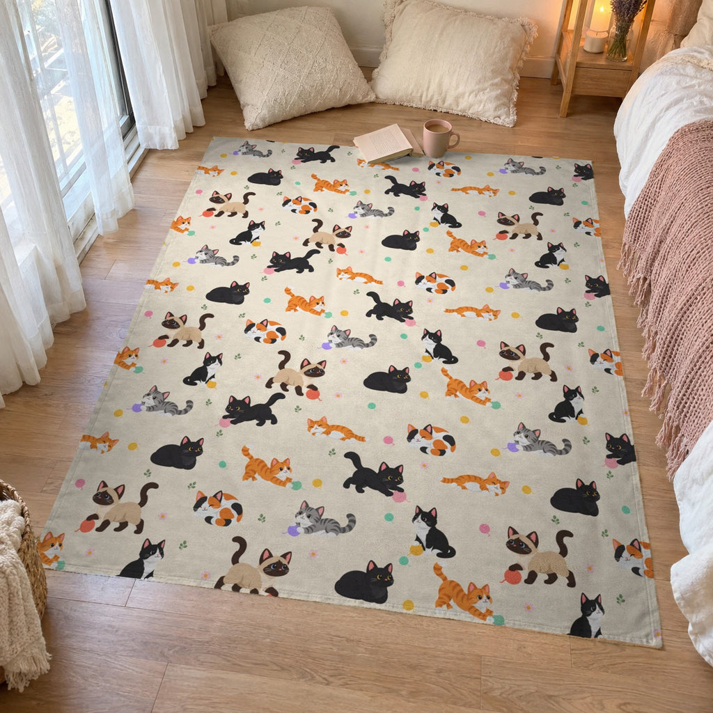 A 50 x 60 inch Cream cat throw blanket in velveteen plush lies on a bedroom floor by a window for an indoor picnic, with pillows, a book and a mug.
